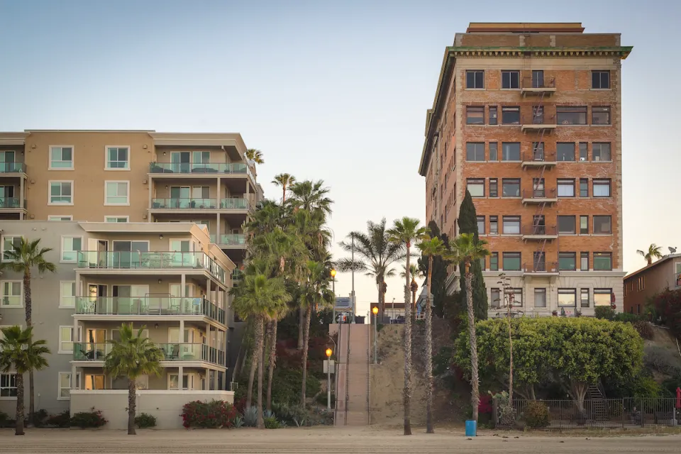 Vintage multi-story brick apartment building and modern concrete and glass apartment building separated by a steep public stairway in Los Angeles, California.
